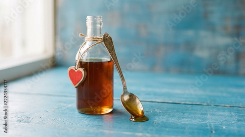 Amber liquid in vintage glass bottle with heart charm and ornate spoon on rustic blue wooden table