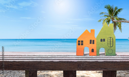 Miniature house on wooden fence over tropical beach background, property and real estate business, summer holiday