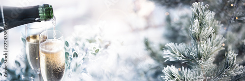 Two filled glasses of champagne and frozen pine branches. Lumious blurred winter background for christmas and new year greetings. Space for text.