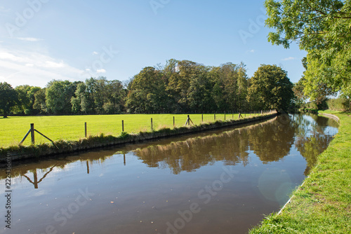 View of an English rural countryside scenery on British waterway canal with blue sky and reflection in autumn fall season