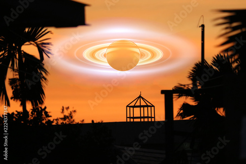 Saturn shadow near earth on the gray sky and silhouette architecture on the sunset orange cloud
