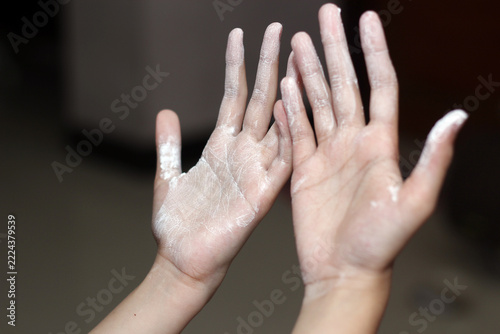 Both palms of a person raised up, covered in fine white powder or flour against a dark background