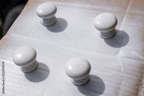 Four white painted knobs rest on cardboard