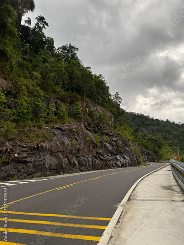 Winding mountain highway passing rocky cliff under cloudy sky