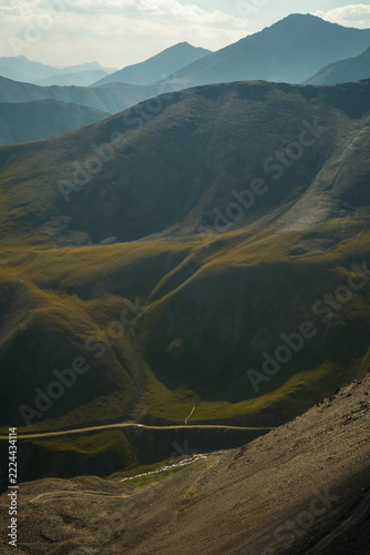 Scenic mountain valley road winding through layered peaks with misty morning light in Ala Too mountains, central Kyrgyzstan.