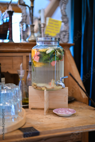 Glass drink dispenser with fruit infused water and mint on a wooden sideboard
