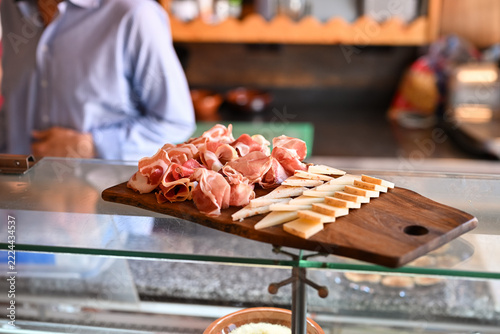 Cured ham and sliced cheese on a wooden board on a deli counter