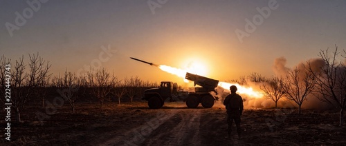 A military rocket launcher unleashes a fiery barrage of missiles against the backdrop of a dramatic sunset, showcasing the intensity of conflict.