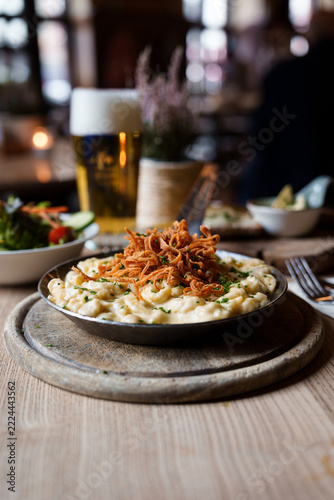 Cheese spaetzle with crispy fried onions in a pan served with salad and beer