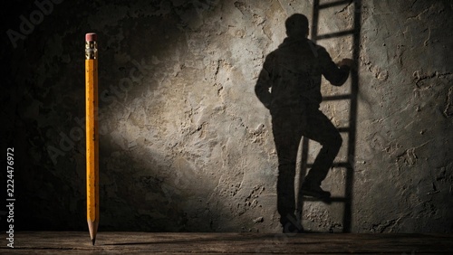 Single yellow pencil casting a shadow of a man climbing a ladder on a concrete wall symbolizing growth and educational success