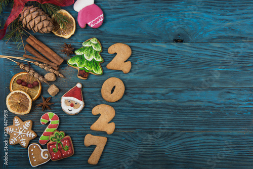 Top view holiday baking concept. Colorful iced biscuits like santa and candy canes with cinnamon and fir on a rustic table dusted with powdered sugar snow. Cozy and festive winter celebration