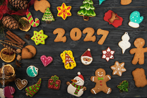 Festive flat lay of homemade iced gingerbread cookies, spices, and pine cones. Holiday baking concept with Santa, snowman, and tree shapes on rustic wood