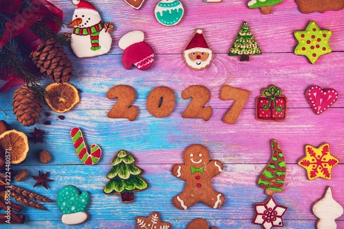 Festive flat lay of homemade iced gingerbread cookies, spices, and pine cones. Holiday baking concept with Santa, snowman, and tree shapes on rustic wood