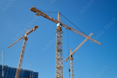 Three yellow industrial tower cranes working on a construction site against a clear blue sky