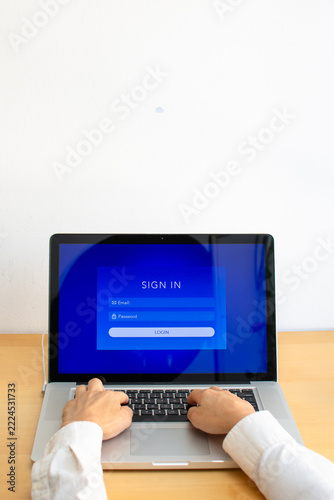 Vertical front view of hands typing on laptop screen showing sign in login interface on desk