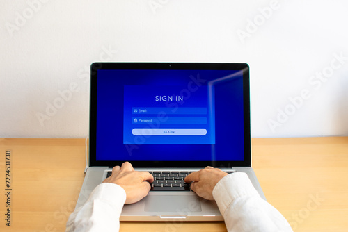 Front view of person typing on laptop keyboard displaying sign in login page on screen