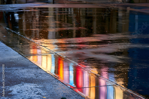 Colorful reflections of urban lights and buildings on a wet street after rain, creating a vibrant, abstract mosaic of city life.