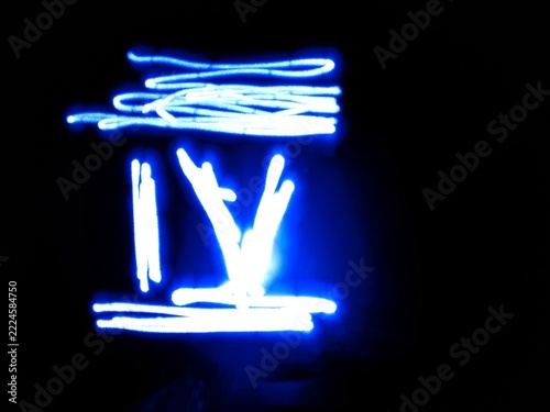 A blue neon light roman four numeral drawn in light painting technique stands out against a pitch black backdrop. This abstract glowing electric digit is ideal for countdown and creative banner.
