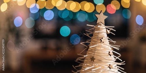 Minimalist White Woven Christmas Tree Ornament with Wooden Stars and Colorful Bokeh Lights Concept