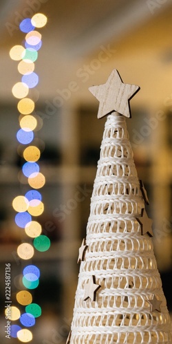 Minimalist White Woven Christmas Tree Ornament with Wooden Stars and Colorful Bokeh Lights Concept