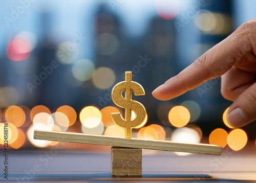A hand gently touches a seesaw with a golden dollar sign on one side, set against a city bokeh background, symbolizing financial balance and decision making.