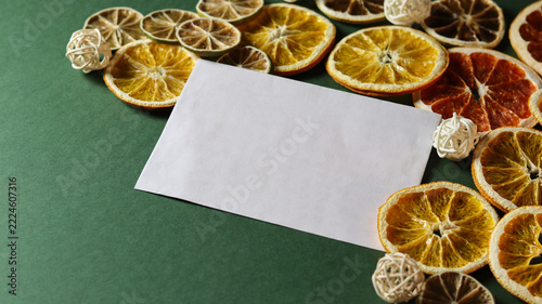 greeting card mockup with blank paper. Dried oranges and white decoration surround a blank piece of paper on a green background