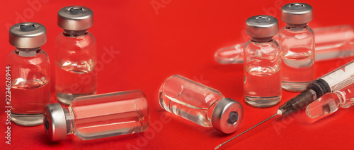 A medication ampoule and a medical needle on a red background.