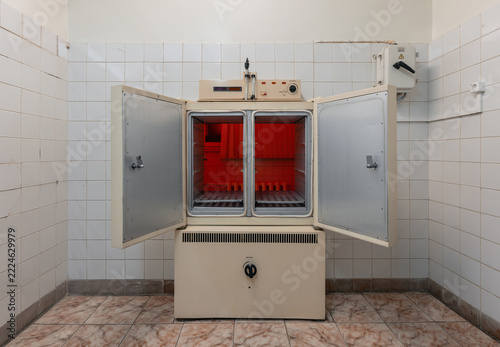 A medical drying cabinet stands with two doors open, revealing perforated shelves and a red-lit space beyond