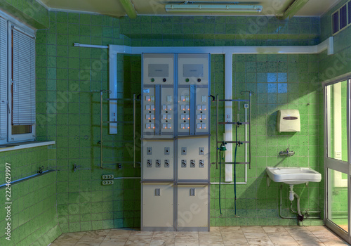 Two vertical medical supply panels with gas outlets and electrical sockets stand beside a sink in a green-tiled hospital room