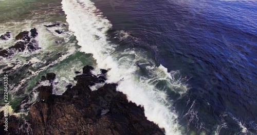 Breaking surf cutting aerial coast, showing jagged rocks, foam, green shore, deep blue ocean