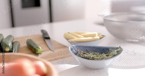 Camera is pulling focus, bringing white-blue herb bowl and knife into mid-ground focus for cooking