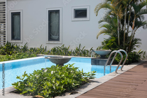 Modern outdoor swimming pool with blue water, decorative stone fountains, palm trees, and wooden deck