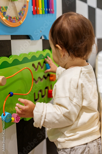Toddler Sliding Blocks Through Maze on Busy Board Wall in Daycare Playroom