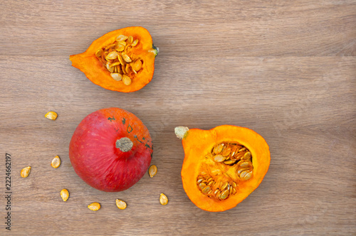 Fresh organic red Hokkaido pumpkin whole, sliced, and seeds on rustic wooden table flat lay with copy space