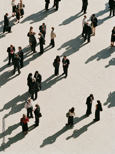People gathering in small groups with long shadows in an overhead crowd view