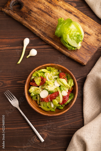 Mixed salad with lettuce, tomatoes, onion in wooden bowl on brown wooden. top view, flat lay, close up
