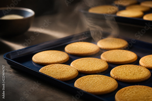 Golden round cookies are cooling on a dark baking tray with steam rising from them.