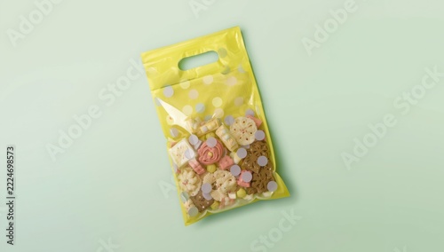 Yellow Plastic Gift Bag Filled with Assorted Cookies and Snacks on a Soft Pastel Green Background