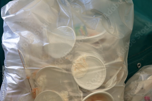 Used disposable plastic plates and cutlery gathered inside a clear garbage bag ready for disposal