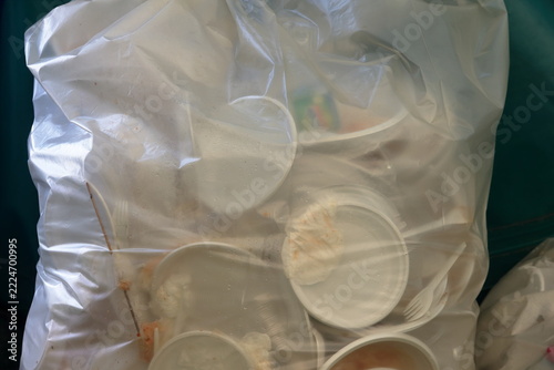 Used disposable plastic plates and cutlery gathered inside a clear garbage bag ready for disposal