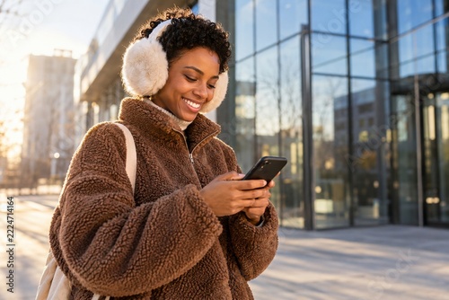 Smiling woman in brown fleece checking her smartphone in warm winter sunlight
