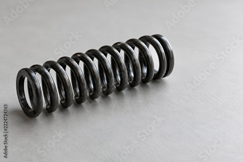 Plain Black Steel Compression Coil Spring on a Light Gray Matte Surface