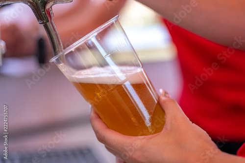 Hand holding plastic cup filling with beer