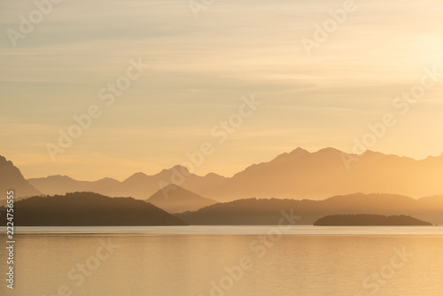 Golden misty mountain layers reflected on calm Patagonian lake at sunrise, Bariloche Argentina serene minimalist landscape concept