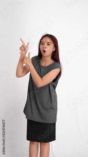 A surprised young woman with long reddish hair pointing upwards while wearing a casual grey top