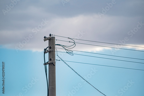 Concrete utility pole with power lines against sky. A cement pole carries multiple wires with insulators under a partly cloudy blue sky. Useful for energy, infrastructure, and editorial projects.