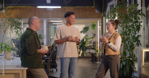Diverse coworkers taking coffee break at office, chatting, sipping coffee, checking phone, smiling