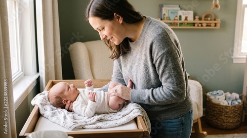 Mother lovingly changing her newborn baby on a changing table in a nursery