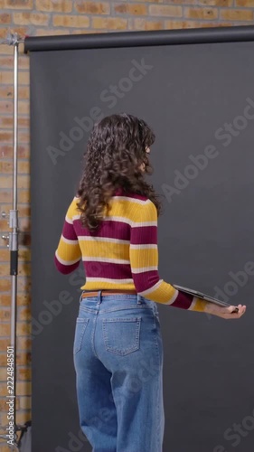 Vertical video: Preparing for shoot, model in striped tee aligning black roll, crew powering light
