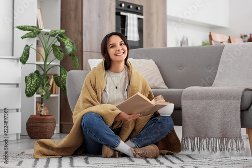 Cozy home lifestyle and relaxation, young woman reading a book wrapped in a w...